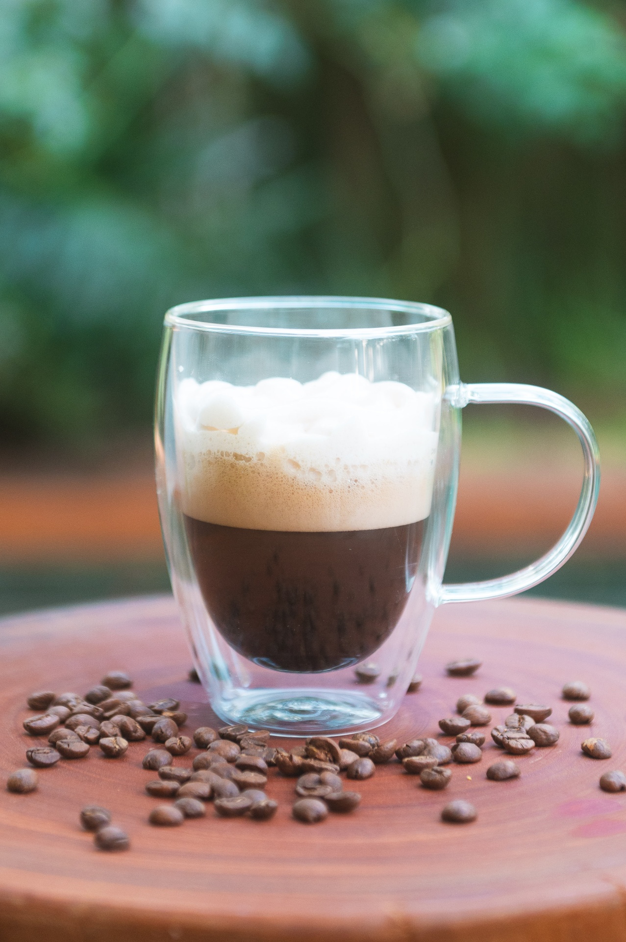 Café cremoso servido em xícara de vidro com grãos ao redor